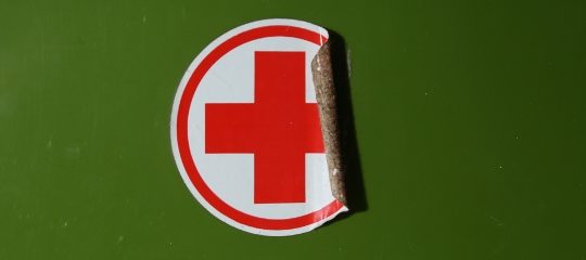 Ein sich teilweise ablösender Aufklber mit Rotem Kreuz vor grünem Untergrund